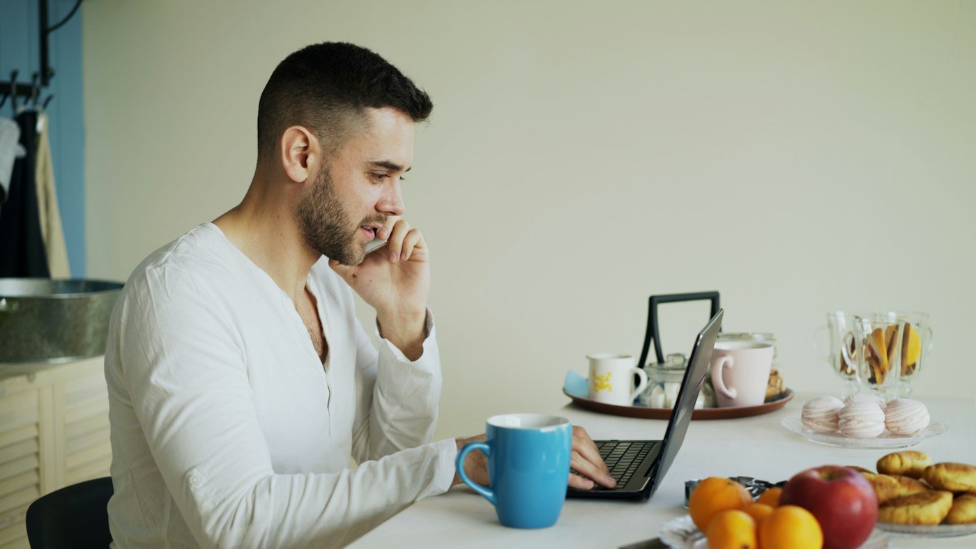 Uomo al computer e al telefono durante una colazione di corsa